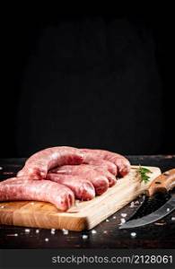 Raw sausages on a wooden cutting board. On a black background. High quality photo. Raw sausages on a wooden cutting board.