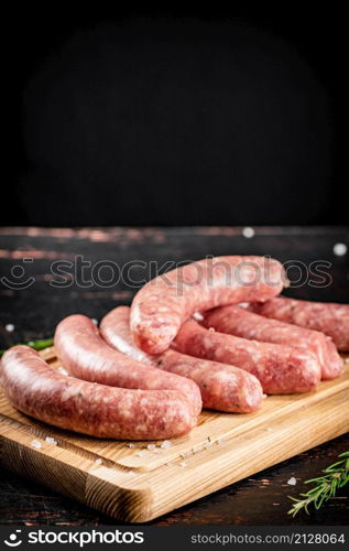 Raw sausages on a wooden cutting board. On a black background. High quality photo. Raw sausages on a wooden cutting board.