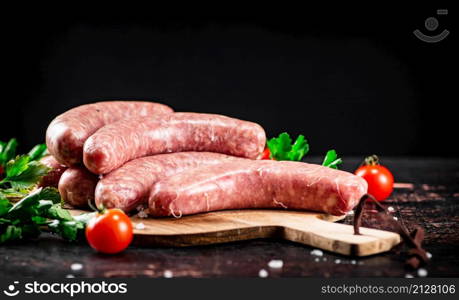 Raw sausages on a wooden cutting board with tomatoes and herbs. Against a dark background. High quality photo. Raw sausages on a wooden cutting board with tomatoes and herbs.