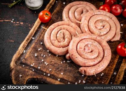 Raw sausages on a wooden cutting board with tomatoes. On a rustic background. High quality photo. Raw sausages on a wooden cutting board with tomatoes.