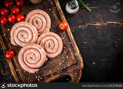 Raw sausages on a wooden cutting board with tomatoes. On a rustic background. High quality photo. Raw sausages on a wooden cutting board with tomatoes.