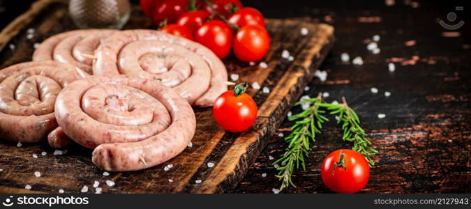 Raw sausages on a wooden cutting board with tomatoes. On a rustic background. High quality photo. Raw sausages on a wooden cutting board with tomatoes.