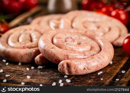 Raw sausages on a wooden cutting board with tomatoes. On a rustic background. High quality photo. Raw sausages on a wooden cutting board with tomatoes.