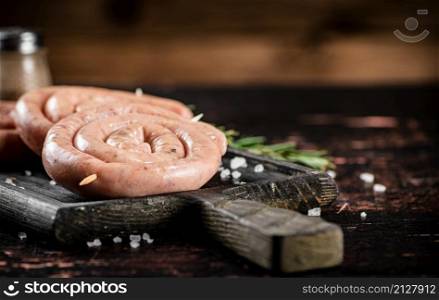 Raw sausages with a sprig of rosemary. On a rustic background. High quality photo. Raw sausages with a sprig of rosemary.