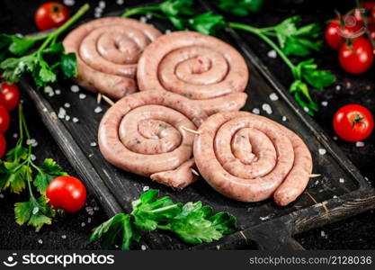 Raw sausages with parsley and tomatoes. On a black background. High quality photo. Raw sausages with parsley and tomatoes.