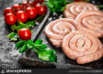 Raw sausages with parsley and tomatoes. On a black background. High quality photo. Raw sausages with parsley and tomatoes.