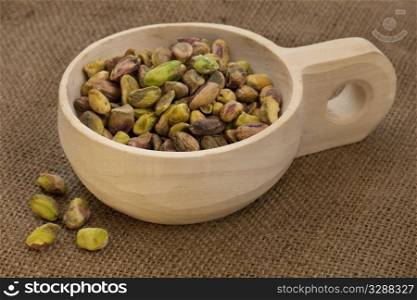raw shelled pistachio nuts on a rustic, wooden scoop with brown burlap background