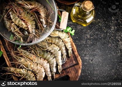 Raw shrimp in a colander and on a cutting board. On a black background. High quality photo. Raw shrimp in a colander and on a cutting board.