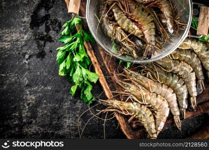 Raw shrimp in a colander and on a cutting board. On a black background. High quality photo. Raw shrimp in a colander and on a cutting board.