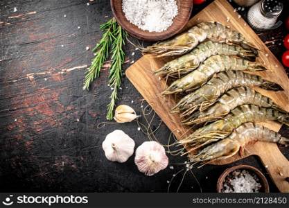 Raw shrimp on a cutting board with garlic and rosemary. Against a dark background. High quality photo. Raw shrimp on a cutting board with garlic and rosemary.