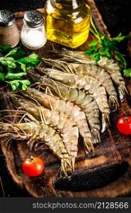 Raw shrimp on a cutting board with herbs and spices. On a black background. High quality photo. Raw shrimp on a cutting board with herbs and spices.