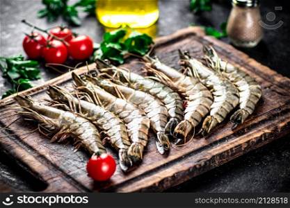Raw shrimp on a cutting board with parsley and tomatoes. On a black background. High quality photo. Raw shrimp on a cutting board with parsley and tomatoes.