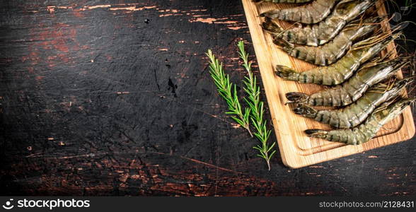 Raw shrimp on a cutting board with rosemary. Against a dark background. High quality photo. Raw shrimp on a cutting board with rosemary.