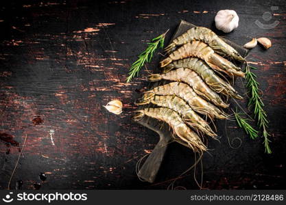 Raw shrimp on a cutting board with rosemary and garlic. Against a dark background. High quality photo. Raw shrimp on a cutting board with rosemary and garlic.