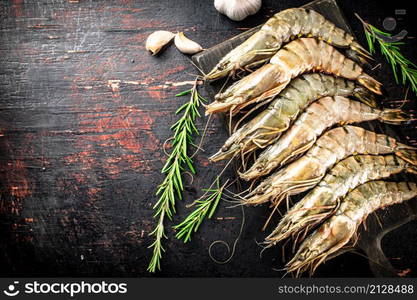 Raw shrimp on a cutting board with rosemary and garlic. Against a dark background. High quality photo. Raw shrimp on a cutting board with rosemary and garlic.