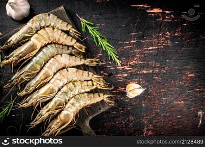 Raw shrimp on a cutting board with rosemary and garlic. Against a dark background. High quality photo. Raw shrimp on a cutting board with rosemary and garlic.