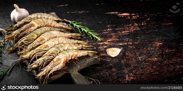 Raw shrimp on a cutting board with rosemary and garlic. Against a dark background. High quality photo. Raw shrimp on a cutting board with rosemary and garlic.