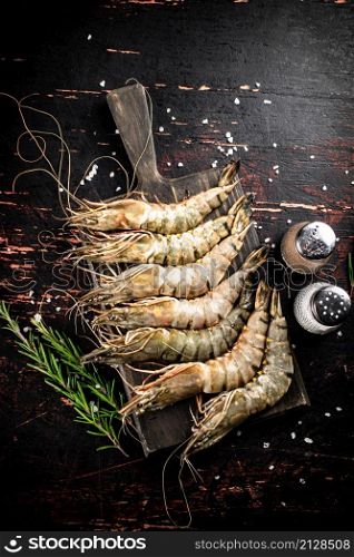 Raw shrimp on a cutting board with spices and rosemary. Against a dark background. High quality photo. Raw shrimp on a cutting board with spices and rosemary.