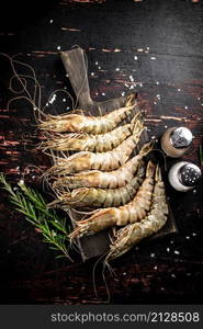 Raw shrimp on a cutting board with spices and rosemary. Against a dark background. High quality photo. Raw shrimp on a cutting board with spices and rosemary.