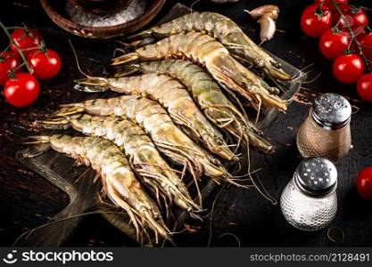 Raw shrimp on a cutting board with spices and tomatoes. Against a dark background. High quality photo. Raw shrimp on a cutting board with spices and tomatoes.