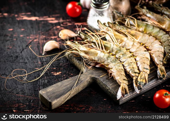 Raw shrimp on a cutting board with spices and tomatoes. Against a dark background. High quality photo. Raw shrimp on a cutting board with spices and tomatoes.