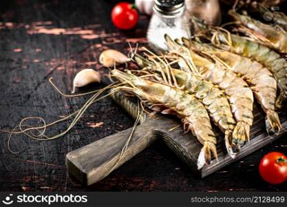 Raw shrimp on a cutting board with spices and tomatoes. Against a dark background. High quality photo. Raw shrimp on a cutting board with spices and tomatoes.