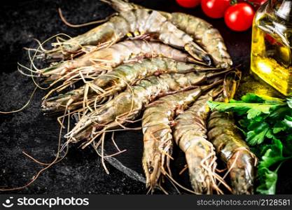 Raw shrimp on a stone board with parsley and tomatoes. On a black background. High quality photo. Raw shrimp on a stone board with parsley and tomatoes.