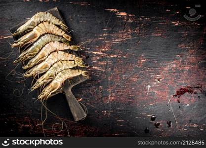 Raw shrimp on a wooden cutting board. On a rustic dark background. High quality photo. Raw shrimp on a wooden cutting board.