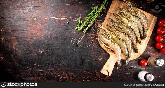 Raw shrimp on a wooden cutting board with tomatoes and spices. Against a dark background. High quality photo. Raw shrimp on a wooden cutting board with tomatoes and spices.