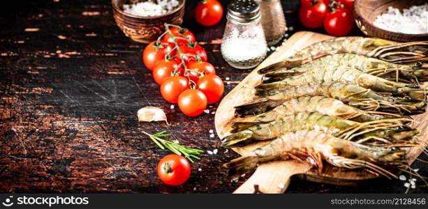 Raw shrimp on a wooden cutting board with tomatoes and spices. Against a dark background. High quality photo. Raw shrimp on a wooden cutting board with tomatoes and spices.