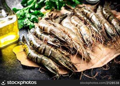 Raw shrimp on paper with parsley and oil. On a black background. High quality photo. Raw shrimp on paper with parsley and oil.