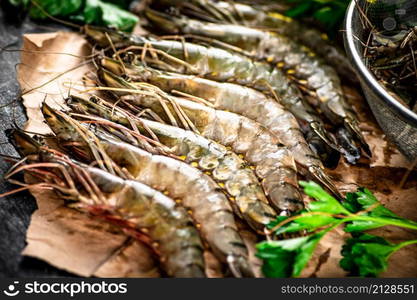 Raw shrimp on paper with spices and parsley. On a black background. High quality photo. Raw shrimp on paper with spices and parsley.