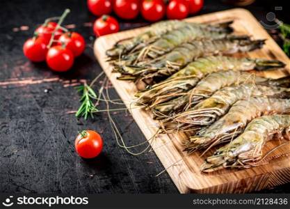 Raw shrimp with cherry tomatoes and rosemary. Against a dark background. High quality photo. Raw shrimp with cherry tomatoes and rosemary.