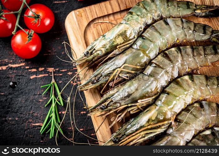Raw shrimp with cherry tomatoes and rosemary. Against a dark background. High quality photo. Raw shrimp with cherry tomatoes and rosemary.