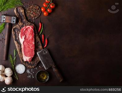 Raw sirloin beef steak in plastic tray with salt and pepper and vintage meat hatchets and hammer on rusty background.Red pepper, tomatoes and garlic.