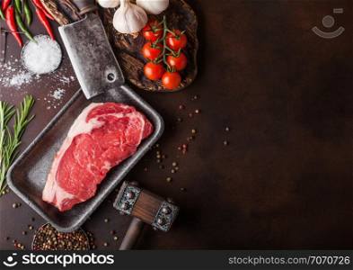 Raw sirloin beef steak in plastic tray with salt and pepper and vintage meat hatchets and hammer on rusty background.Red pepper, tomatoes and garlic.