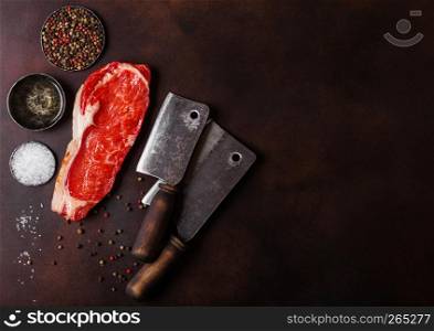 Raw sirloin beef steak with vintage meat hatchets on rusty background. Salt and pepper with fresh rosemary and bowl of oil
