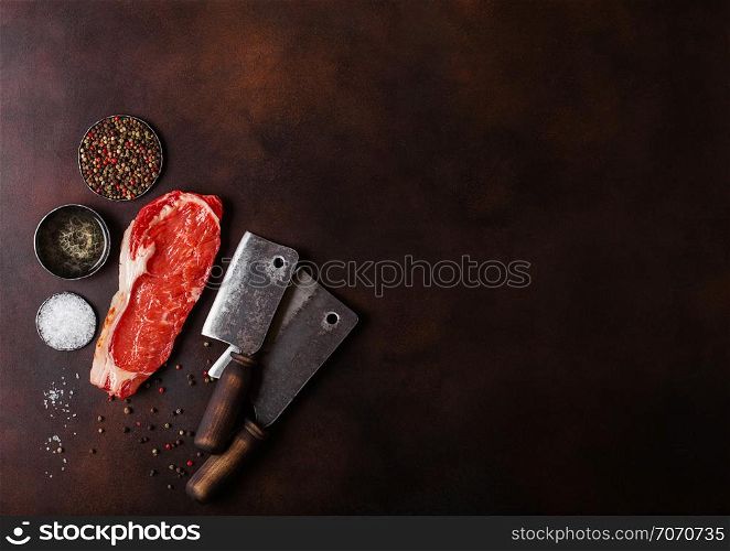 Raw sirloin beef steak with vintage meat hatchets on rusty background. Salt and pepper with fresh rosemary and bowl of oil
