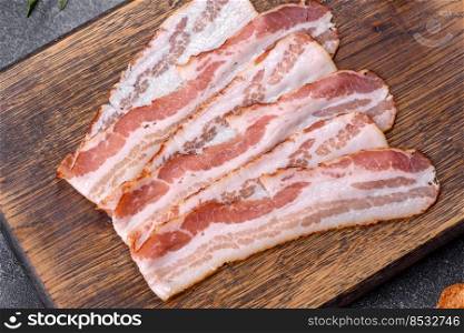 Raw smoked bacon on a wooden board with several cut pieces. Raw smoked bacon slices on a wooden board with spices and herbs
