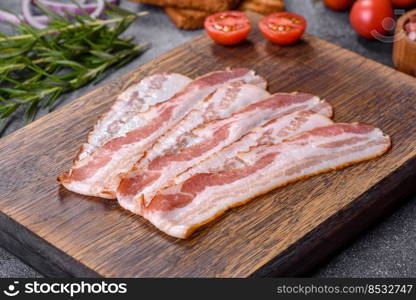 Raw smoked bacon on a wooden board with several cut pieces. Raw smoked bacon slices on a wooden board with spices and herbs