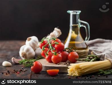 Raw spaghetti pasta with cherry tomatoes, olive oil with garlic and rosemary on wooden background kitchen linen towel