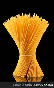 Raw spaghetti tied in a sheaf stands on a dark glass on a black background. whole grain italian spaghetti pasta