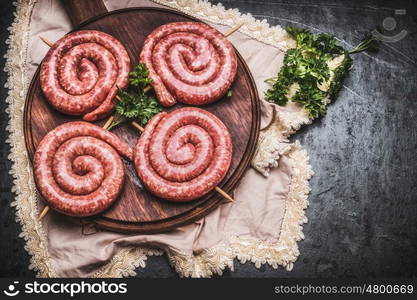 Raw spiral sausages on wooden cutting board, top view, place for text