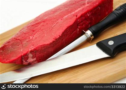 Raw Steak An Knife. A large uncooked steak on a cutting board with butcher knife and sharpener on a white background