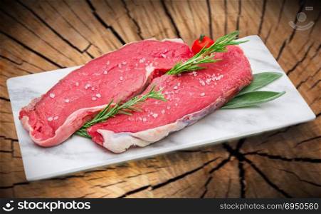 raw steak meat on white dish with tree trunk background
