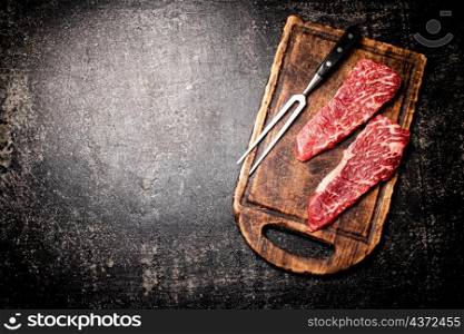 Raw steak on a cutting board. On a black background. High quality photo. Raw steak on a cutting board.