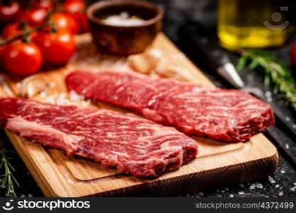 Raw steak on a wooden cutting board. On a black background. High quality photo. Raw steak on a wooden cutting board.