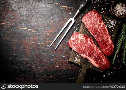 Raw steak on a wooden cutting board with spices. On a rustic dark background. High quality photo. Raw steak on a wooden cutting board with spices.