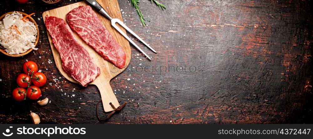 Raw steak on a wooden cutting board with spices. On a rustic dark background. High quality photo. Raw steak on a wooden cutting board with spices.