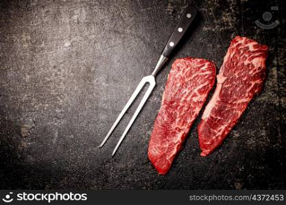 Raw steak with fork on the table. On a black background. High quality photo. Raw steak with fork on the table.